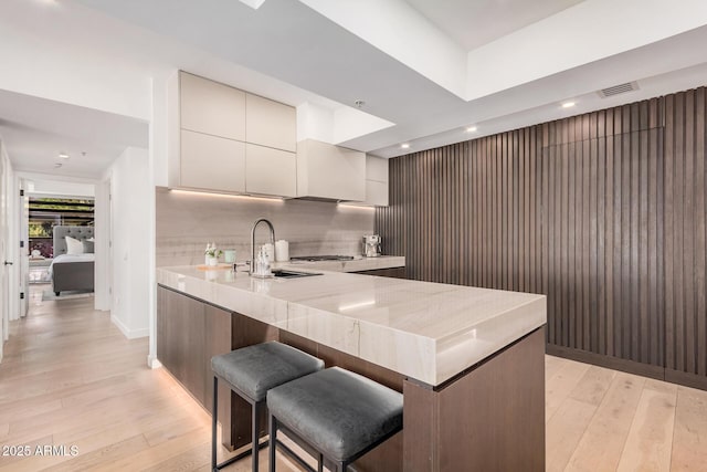 kitchen featuring light wood finished floors, modern cabinets, a sink, a peninsula, and light stone counters