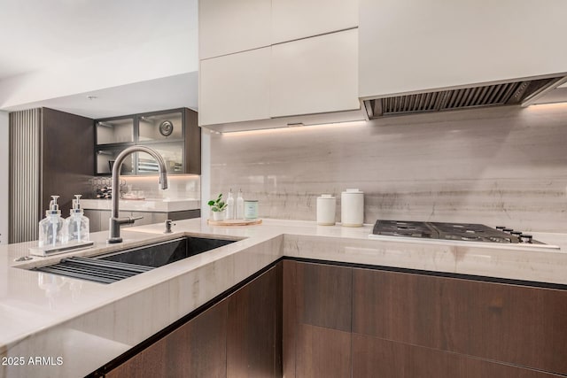 kitchen featuring a sink, stainless steel gas stovetop, range hood, backsplash, and dark brown cabinets