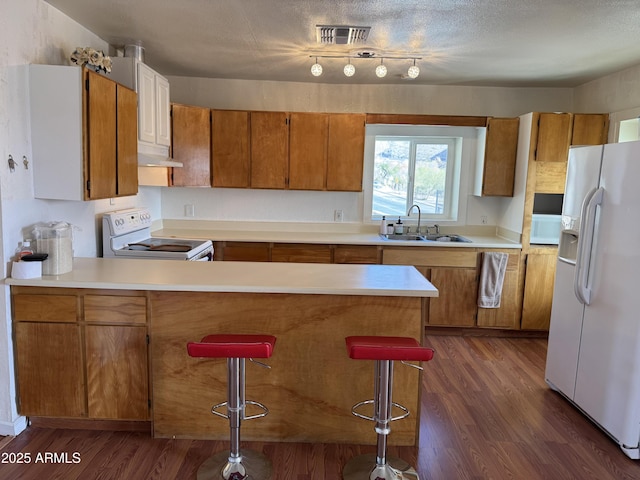 kitchen featuring sink, white appliances, a breakfast bar area, dark wood-type flooring, and kitchen peninsula