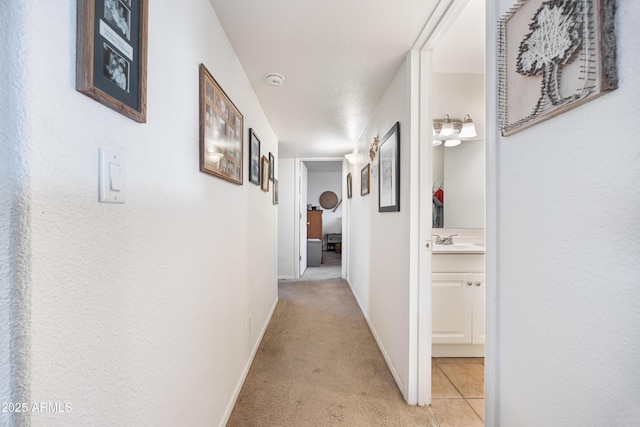 corridor featuring baseboards, light tile patterned floors, a sink, and light colored carpet