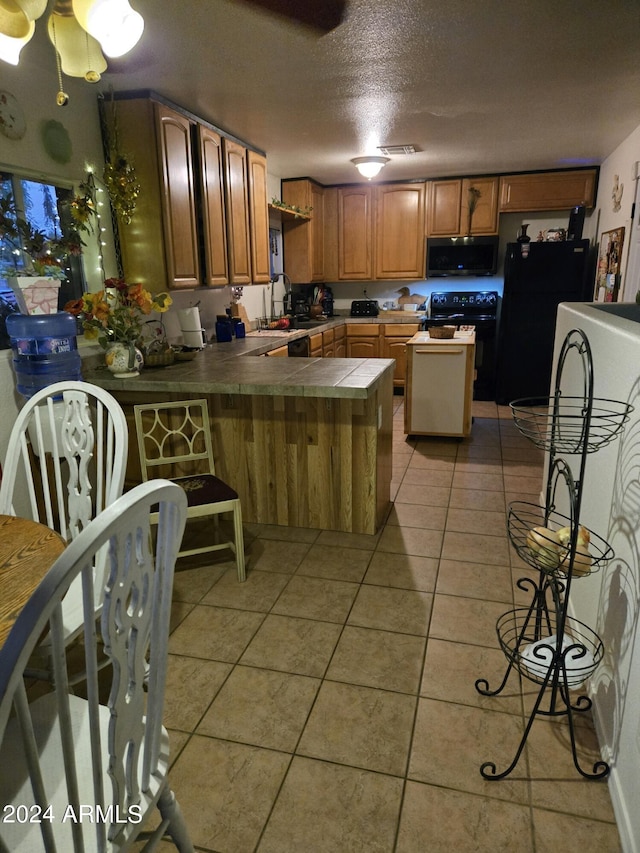 kitchen featuring light tile patterned floors, tile countertops, a peninsula, a sink, and black appliances