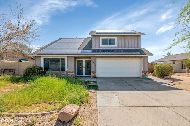 traditional-style home featuring driveway, french doors, solar panels, fence, and an attached garage
