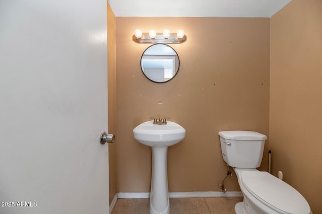 half bath with tile patterned flooring, a sink, baseboards, and toilet