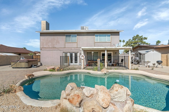 view of swimming pool featuring a hot tub, a shed, a fenced backyard, a patio area, and an outdoor structure
