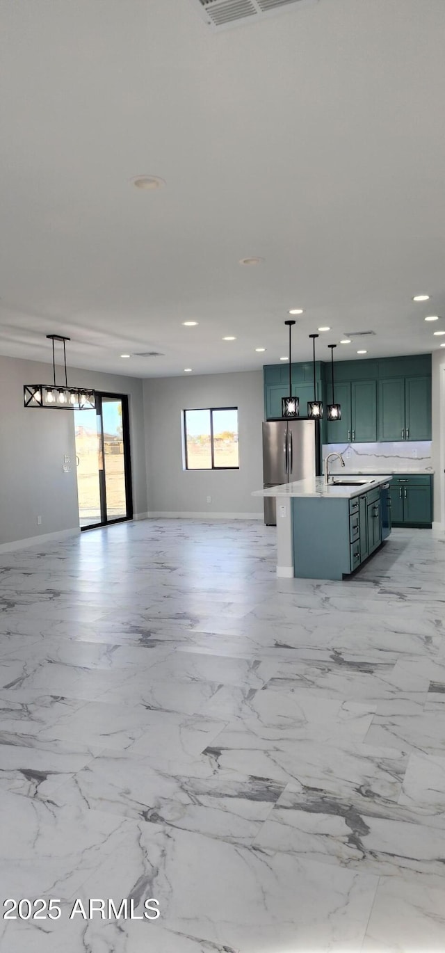 kitchen featuring pendant lighting, sink, a center island with sink, and stainless steel refrigerator