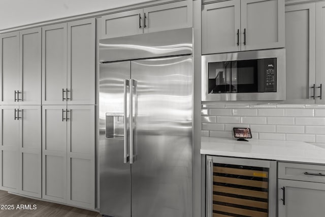 kitchen featuring wine cooler, gray cabinets, built in appliances, and light stone countertops