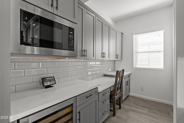 kitchen featuring gray cabinetry, light stone counters, built in microwave, decorative backsplash, and beverage cooler