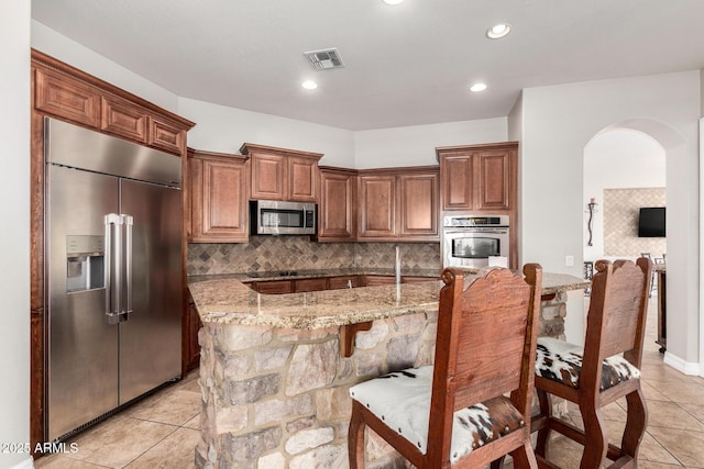 3824 E Parkside Ln, Phoenix, AZ 85050 - kitchen featuring stainless steel appliances, arched walkways, light stone counters, tasteful backsplash, and light tile patterned floors