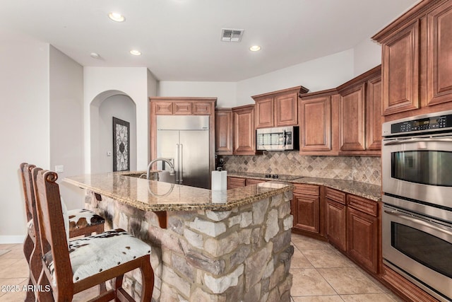 3824 E Parkside Ln, Phoenix, AZ 85050 - kitchen with appliances with stainless steel finishes, backsplash, arched walkways, stone countertops, and a kitchen bar