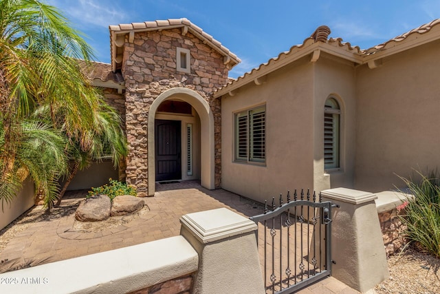 3824 E Parkside Ln, Phoenix, AZ 85050 - view of exterior entry featuring a tiled roof, stucco siding, stone siding, a gate, and a patio