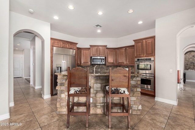 3824 E Parkside Ln, Phoenix, AZ 85050 - kitchen with appliances with stainless steel finishes, arched walkways, tasteful backsplash, light stone countertops, and a breakfast bar area