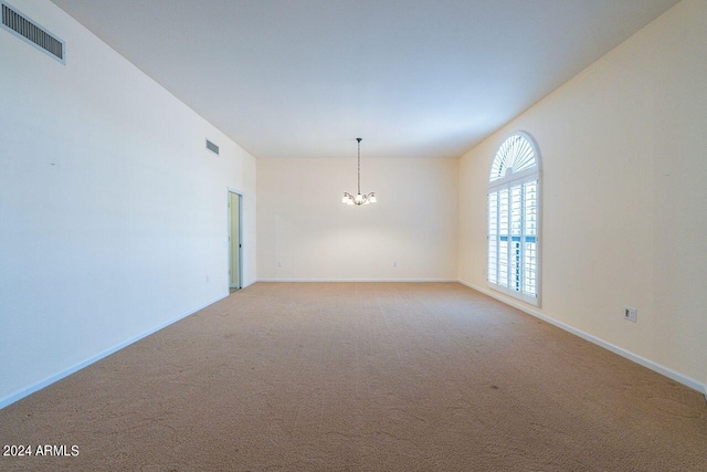 carpeted spare room with an inviting chandelier