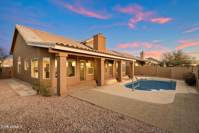 back house at dusk featuring a fenced in pool and a patio