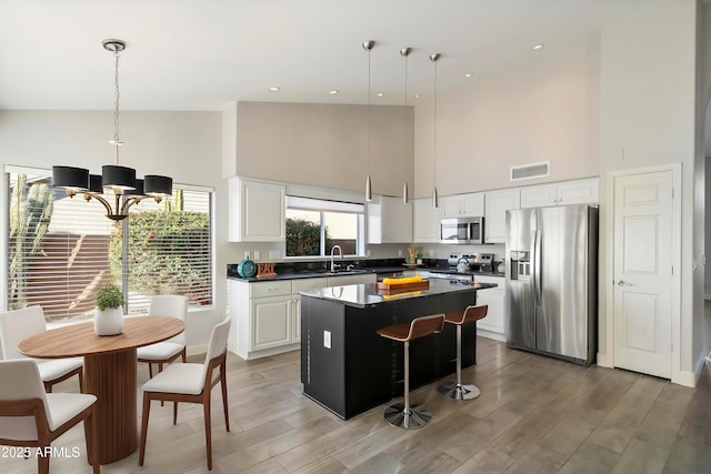 kitchen with white cabinetry, decorative light fixtures, a kitchen island, and appliances with stainless steel finishes