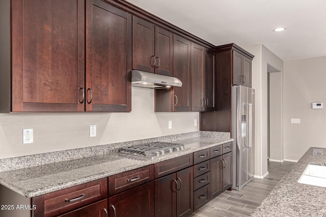 kitchen featuring dark brown cabinetry, appliances with stainless steel finishes, light stone counters, light wood-style floors, and under cabinet range hood