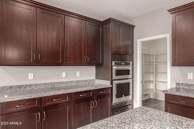 kitchen with dark brown cabinets, light stone counters, wood finished floors, and double oven