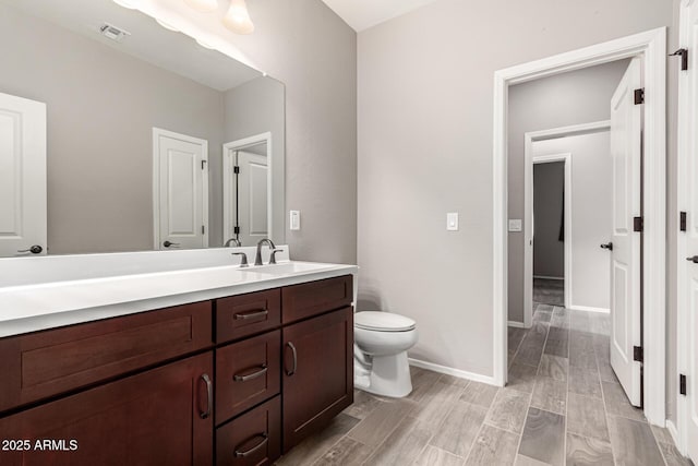 bathroom with vanity, toilet, baseboards, wood finished floors, and visible vents