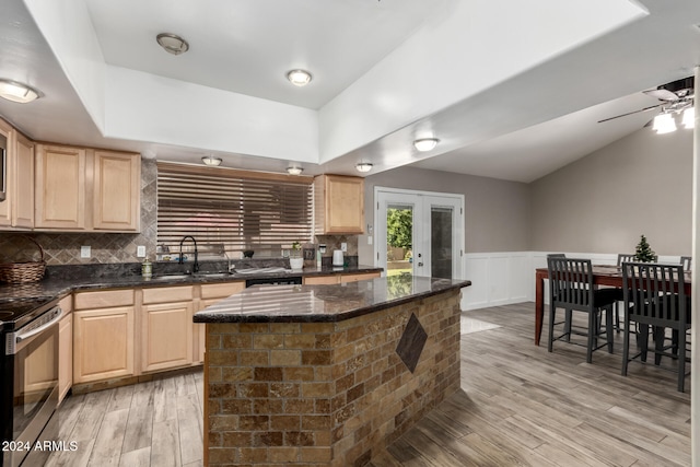 kitchen with light brown cabinets, tasteful backsplash, light hardwood / wood-style flooring, stainless steel electric stove, and a kitchen island