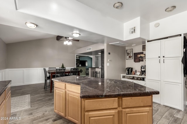 kitchen with light brown cabinets, dark stone counters, ceiling fan, light wood-type flooring, and a kitchen island