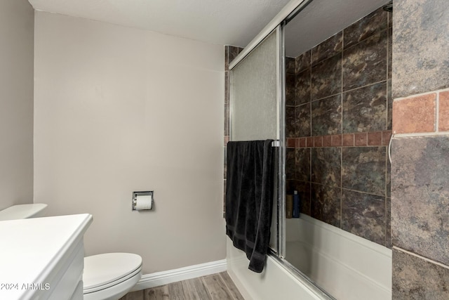 full bathroom with hardwood / wood-style floors, vanity, toilet, and bath / shower combo with glass door