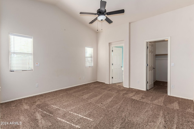 unfurnished bedroom featuring dark carpet, a walk in closet, vaulted ceiling, and ceiling fan