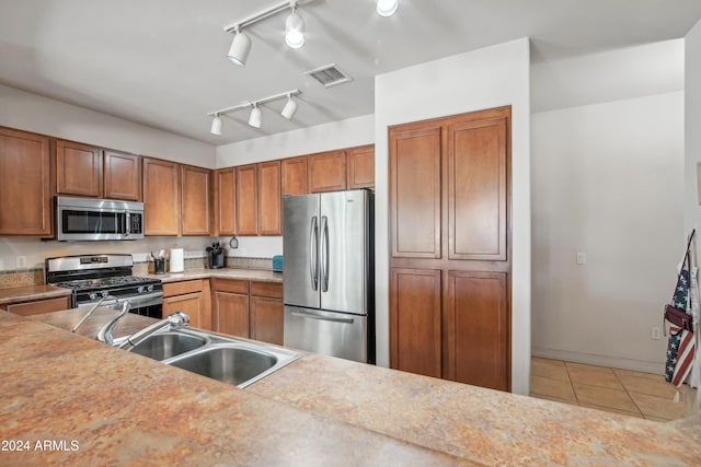 kitchen featuring brown cabinets, visible vents, appliances with stainless steel finishes, light tile patterned flooring, and a sink