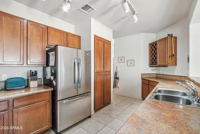 kitchen with visible vents, brown cabinetry, freestanding refrigerator, a sink, and light tile patterned flooring