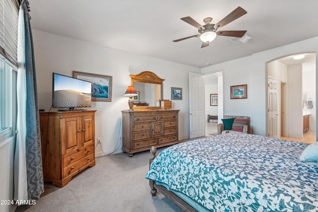 carpeted bedroom featuring arched walkways, ensuite bath, and a ceiling fan