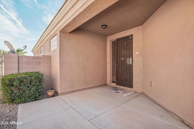 view of exterior entry featuring a patio area, fence, and stucco siding