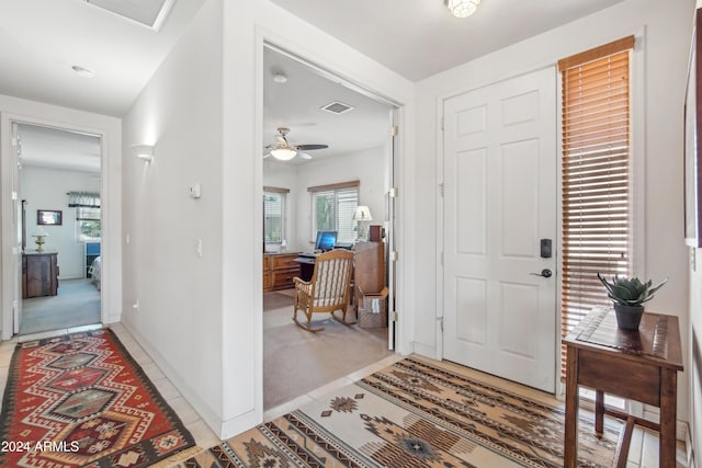 entryway featuring light carpet, ceiling fan, visible vents, and baseboards