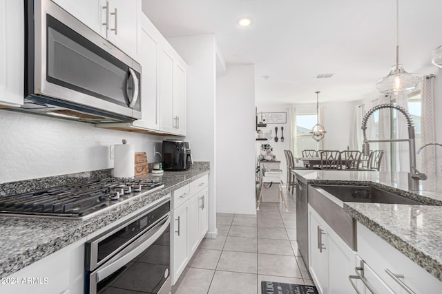 kitchen featuring pendant lighting, white cabinets, appliances with stainless steel finishes, light tile patterned floors, and light stone countertops