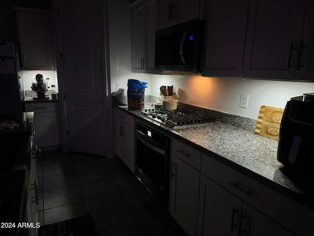 kitchen featuring dark stone countertops, oven, dark tile patterned floors, and stainless steel gas cooktop