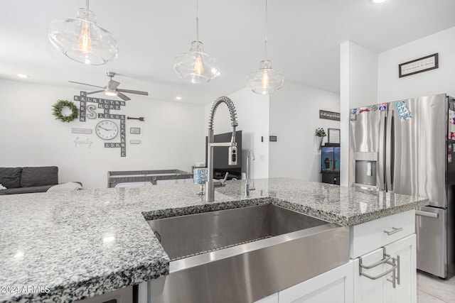 kitchen with hanging light fixtures, white cabinetry, light stone counters, ceiling fan, and sink