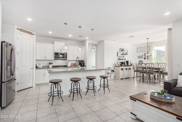 kitchen featuring an island with sink, stainless steel appliances, white cabinets, and decorative light fixtures