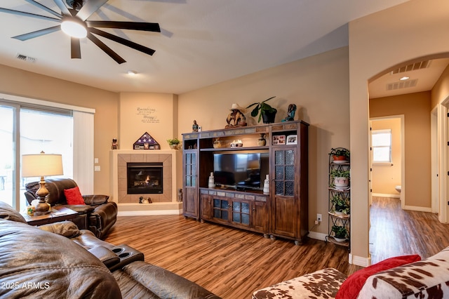 living area with visible vents, a tiled fireplace, ceiling fan, wood finished floors, and baseboards