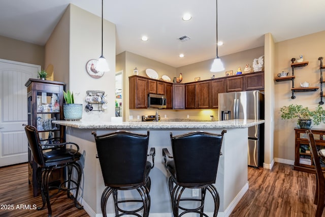 kitchen with visible vents, appliances with stainless steel finishes, dark wood-style flooring, hanging light fixtures, and a kitchen bar