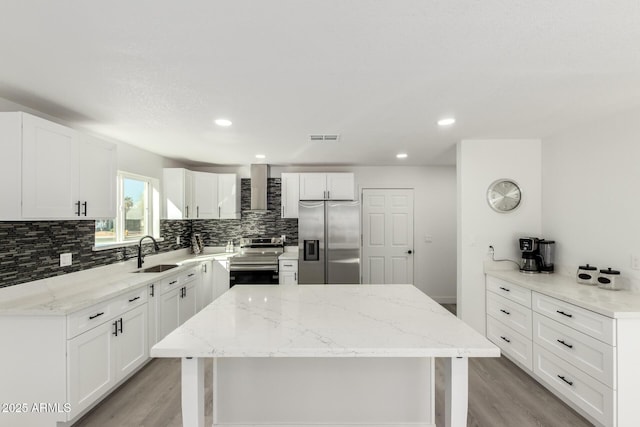 kitchen featuring white cabinets, wall chimney exhaust hood, stainless steel appliances, and a sink