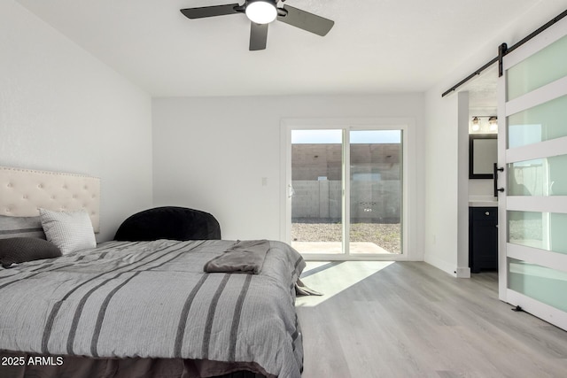 bedroom with ceiling fan, a barn door, access to exterior, light wood finished floors, and ensuite bath