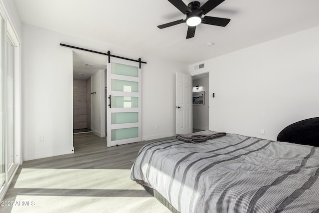 bedroom with wood finished floors, visible vents, baseboards, and a barn door