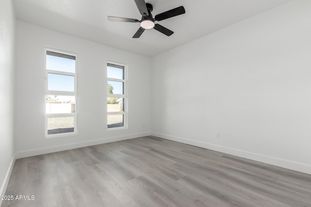 spare room featuring ceiling fan, light wood-style flooring, and baseboards