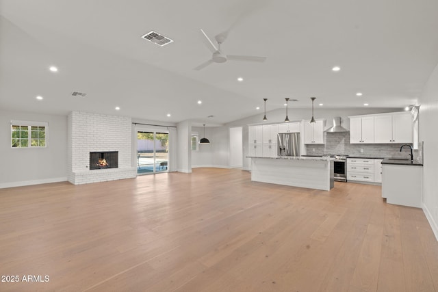 unfurnished living room with a brick fireplace, plenty of natural light, light hardwood / wood-style floors, and vaulted ceiling