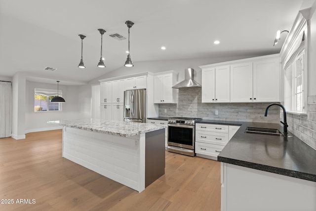 kitchen featuring wall chimney range hood, white cabinetry, hanging light fixtures, stainless steel appliances, and a center island