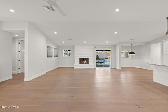 unfurnished living room with vaulted ceiling, ceiling fan, light hardwood / wood-style floors, and a brick fireplace