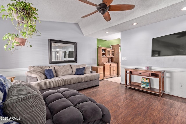 living area featuring ceiling fan, a textured ceiling, wood finished floors, lofted ceiling, and a wainscoted wall