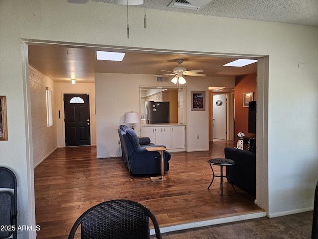 living area with wood finished floors, a ceiling fan, visible vents, and a skylight