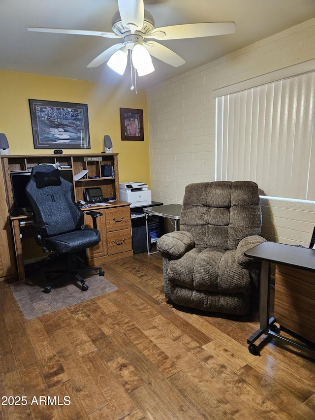 home office featuring wood finished floors, a ceiling fan, and concrete block wall