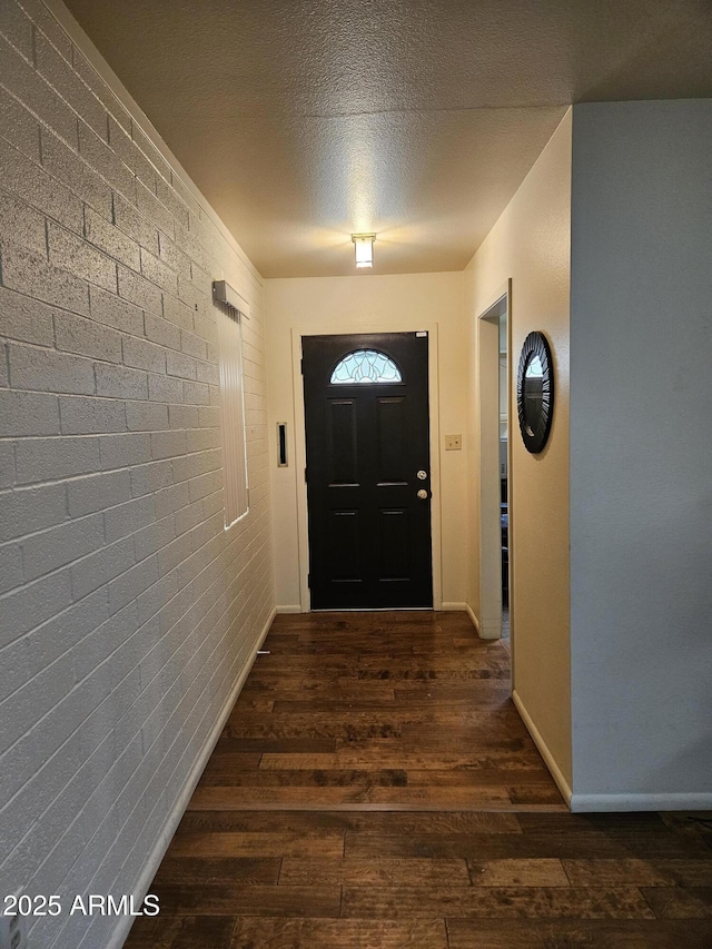 doorway featuring a textured ceiling, brick wall, hardwood / wood-style floors, and baseboards