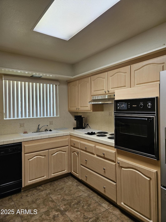 kitchen with a sink, tile counters, under cabinet range hood, black appliances, and light brown cabinetry