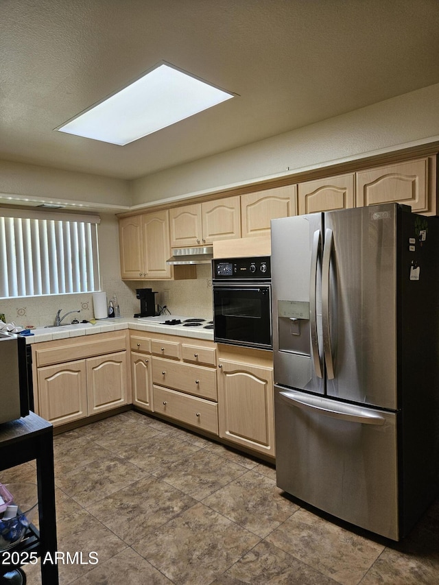 kitchen with light brown cabinetry, stainless steel refrigerator with ice dispenser, black oven, and under cabinet range hood