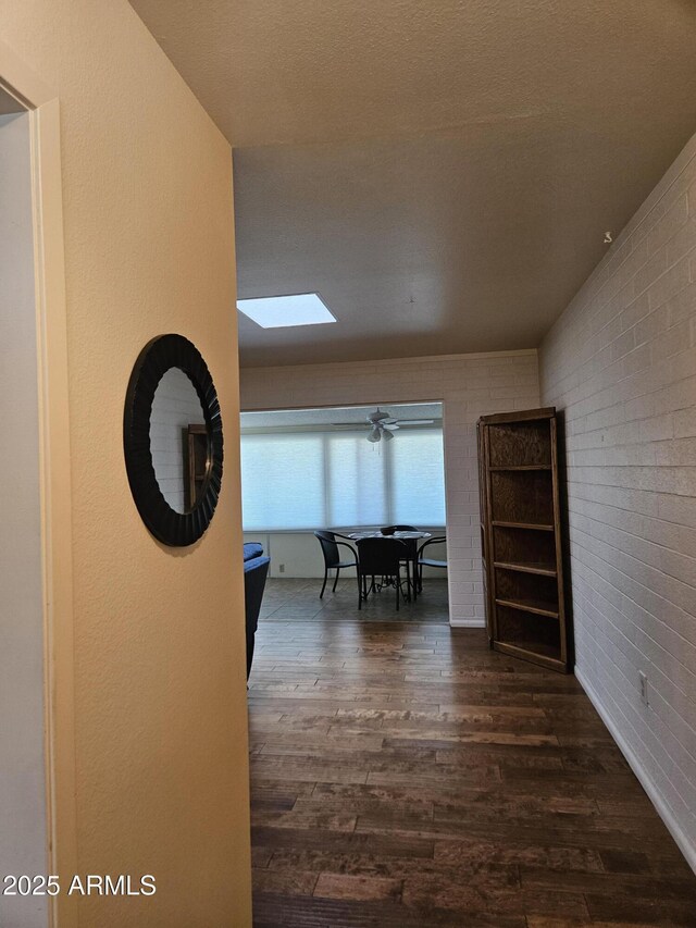 hall with brick wall, a skylight, and dark wood-type flooring